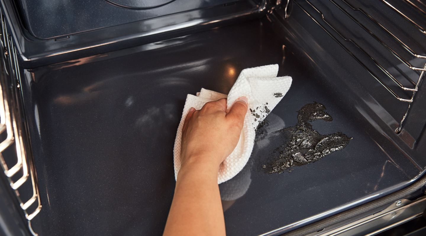 Hand holding paper towel wiping residue off of bottom of oven cavity Hand holding paper towel wiping residue off of bottom of oven cavity