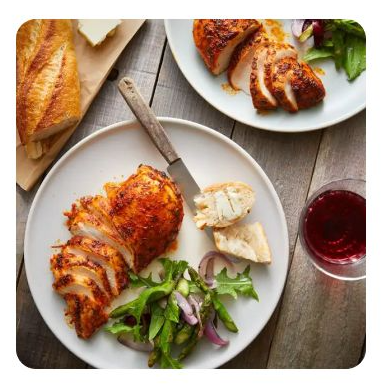A plate of sliced, seasoned chicken breast with a side salad and bread