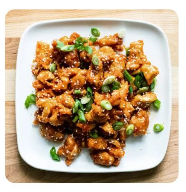 Saucy chicken pieces on a plate with sesame seeds and chopped scallions