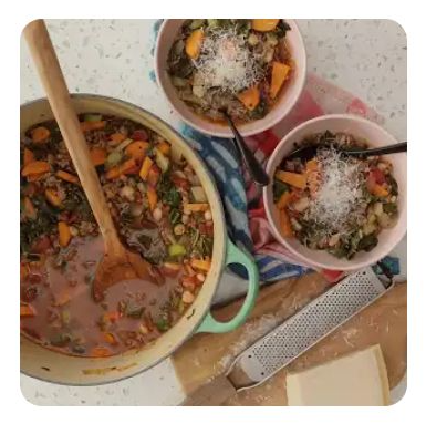 A pot and two bowls of vegetable beef soup with grated cheese