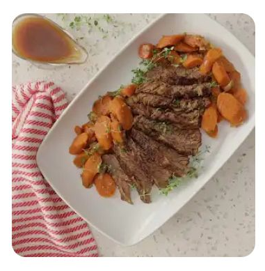 A white serving dish with sliced brisket, carrots and gravy