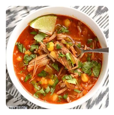 A bowl of tomato-based soup with shredded pork and herbs