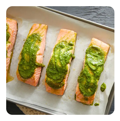 Salmon filets on a baking sheet topped with green pesto spread