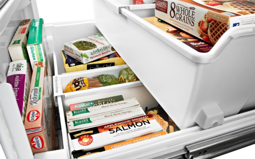 A variety of frozen groceries in the freezer compartment of a white refrigerator