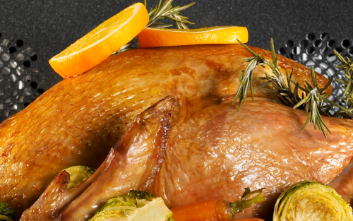 A turkey cooking in an oven garnished in rosemary and orange slices