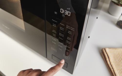 Close up of a person pressing buttons on a black microwave