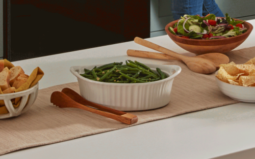 Ceramic pot of cooked green beans next to salads and breads