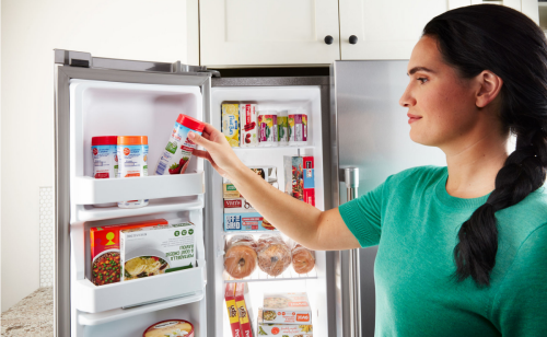 A woman pulling frozen fruit out of the freezer compartment of a French door fridge