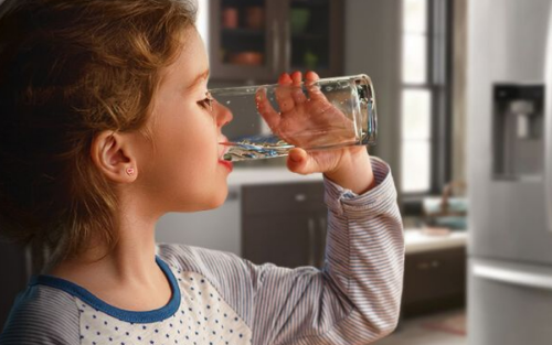 A young girl drinking out of a glass of water