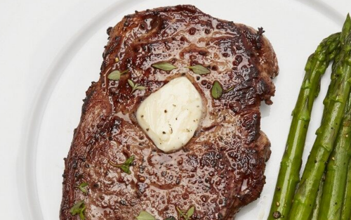 A butter garnished steak dish with asparagus on the side