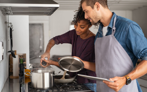 A man and woman cooking together at a range