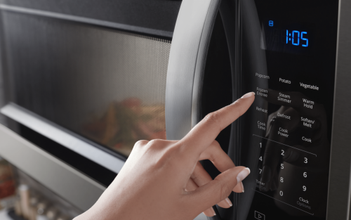 A closeup of a person’s hand programming a setting on a Whirlpool® microwave.