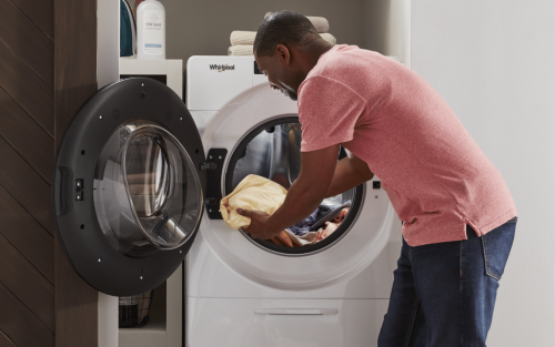 Person placing clothes into a Whirlpool® front load dryer.