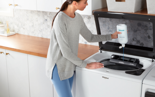 Woman pouring Swash® laundry detergent into a top load washer