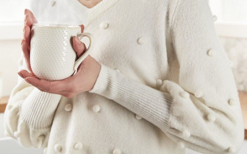 Person in a white sweater holding a white mug