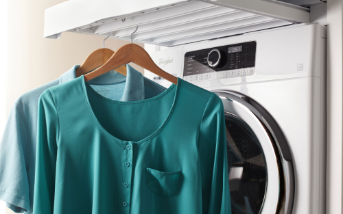 Two freshly dried shirts hanging in front of a Whirlpool® washing machine