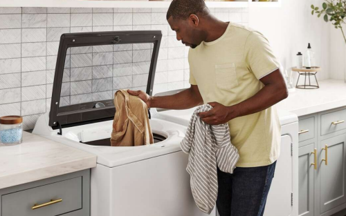 Person loading clothes into a white top load washer