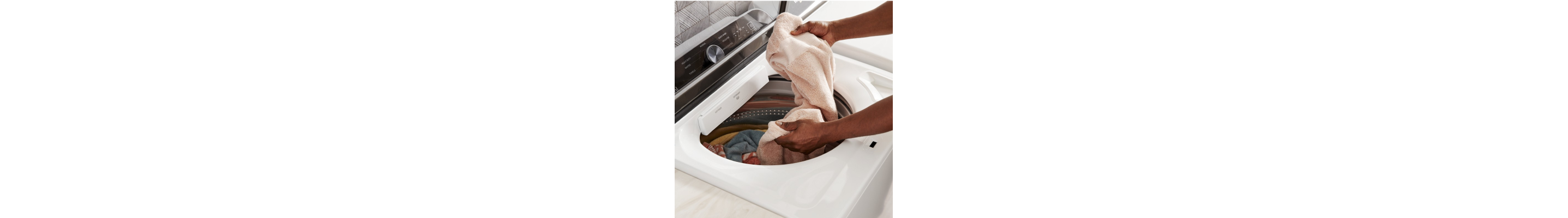 Person loading towels into a white top-load washer
