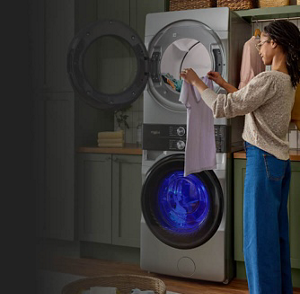 A person holding up a white shirt next to a stacked washer and dryer