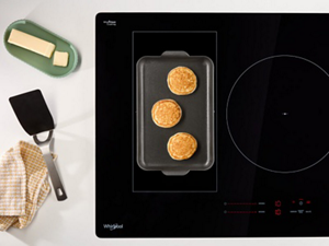 An overhead view of an induction cooktop with pancakes on the griddle