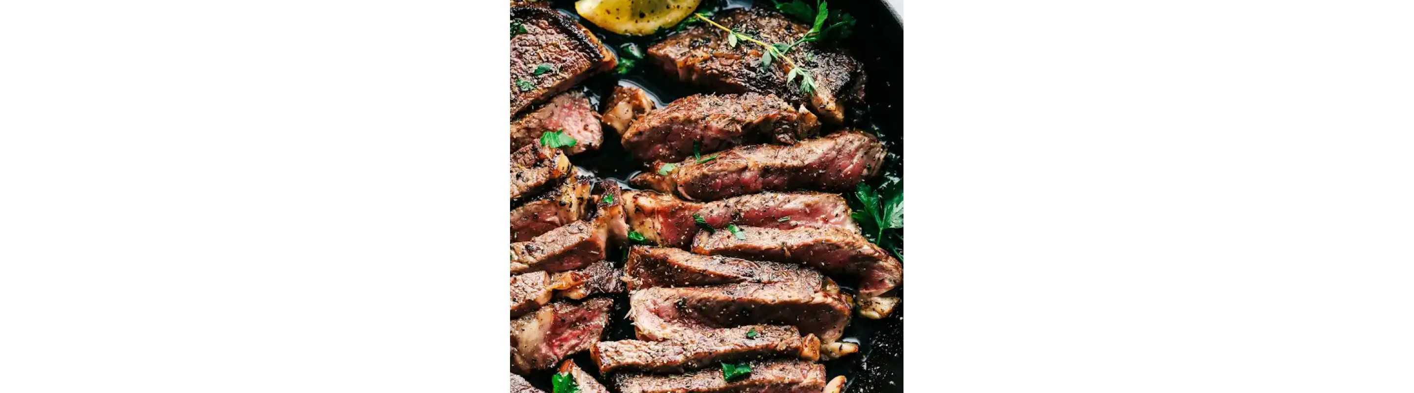 Thinly sliced steak pieces in a skillet garnished with a lemon wedge