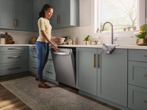 A person standing in their kitchen using one hand to close their dishwasher