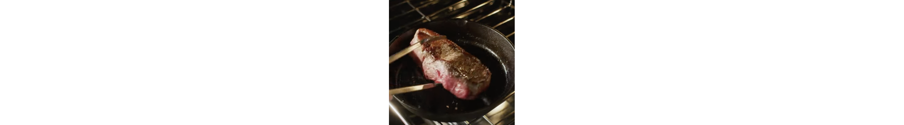 A pair of tongs arranging a steak on a skillet