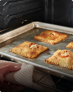 A person pulling a tray of food out of a Whirlpool® Range